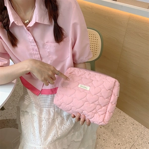 Detail showing pink quilted heart makeup bag with logo held in hand in a lifestyle setting