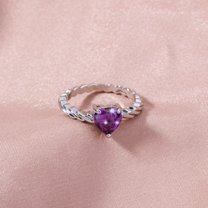 Close-up of heart-shaped purple gemstone ring with twisted silver band on pink silk