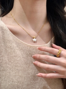 Gros plan du collier perle étoile dorée et bague fleurie sur mannequin en maille