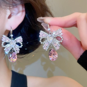Close-up of pink and white zircon bow earrings with drop pendants on a model