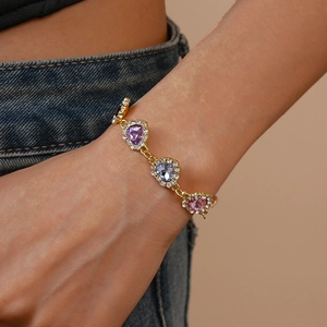 Gros plan du bracelet doré avec pierres de cœur colorées et diamants sur le poignet
