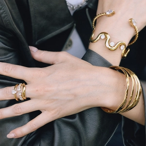 Close-up of gold stainless steel zircon ring and bracelets on a leather jacket sleeve