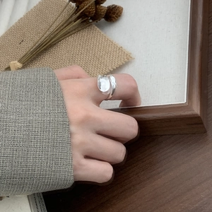 Close-up of minimalist silver irregular open ring worn on finger against wooden frame