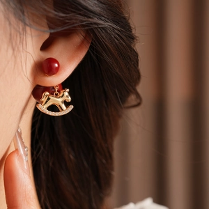 Detail of gold rocking horse earring with red bead and clear crystals worn by a model