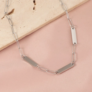 Silver paperclip chain necklace with rectangular bar pendants on silk background