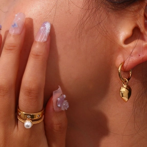 Detail shot of gold heart pendant earrings and layered pearl ring on a model