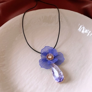 Détail du pendentif fleur avec pétales bleus, cristal goutte violet et cordon en cire noire