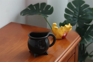 Close-up of a glossy black ceramic cauldron mug with a unique three-footed tripod base