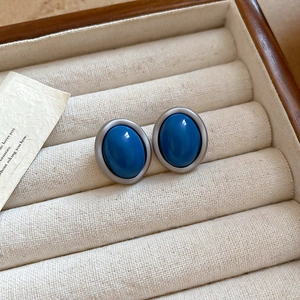 Macro detail of dark blue oval stud earrings with matte silver frames in a jewelry box