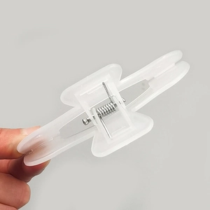 Transparent white plastic book clip with strong metal spring held by hand in a grey studio