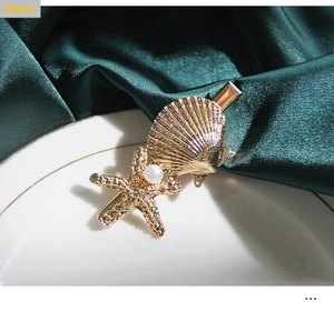 Detail view of golden starfish and shell hair clip with white pearl on silk fabric