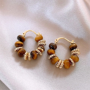 Detail of leopard print earrings with tiger eye beads on beige silk fabric background