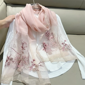 Pink sheer scarf with floral embroidery and gold trim hanging on a white shirt