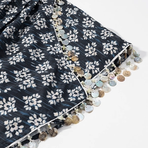 Détail de la jupe bleu marine à imprimé floral avec des finitions à franges en coquillages