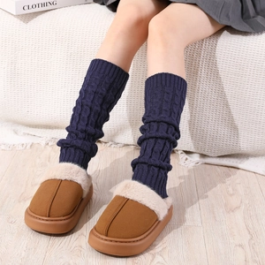 Close-up of cable knit leg warmers in navy blue and brown plush winter slippers