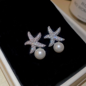 Gros plan de boucles d'oreilles étoile de mer avec zircons et perles sur velours noir