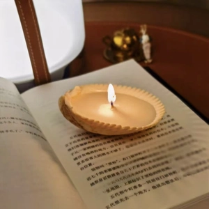Scented shell-shaped candle in pale yellow burning on an open book with cozy vibes