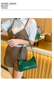 Close-up of emerald green crocodile pattern leather underarm bag held by a model