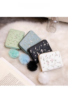 Detailed embroidery on four compact zip wallets in mint, blue, black, and white colors
