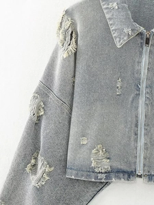 Close-up of light blue denim jacket featuring distressed ripped details and metal zipper