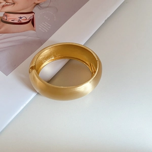 Macro detail of matte gold bangle showing brushed texture and hinge closure mechanism