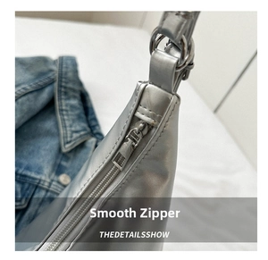 Detail of silver metallic bag showing smooth zipper closure and hardware on denim fabric
