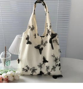 Detail of elegant black butterfly and flower embroidery on off-white canvas tote bag