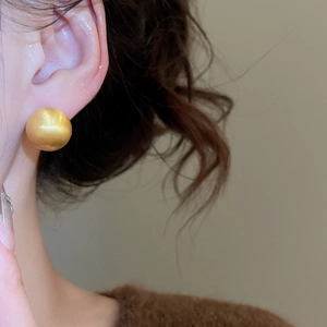 Close-up of golden brushed sphere stud earring worn on earlobe for a minimalist look