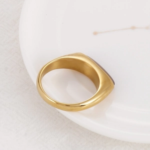 Close-up of golden stainless steel signet ring with a dark brown inset on white ceramic