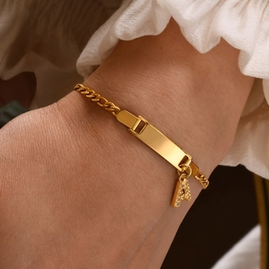 Detail of gold Cuban link bracelet with engravable rectangular bar and diamond letter A charm