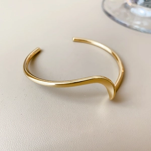 Close-up of a wavy gold-plated open bangle with a polished irregular metallic finish