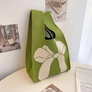 Detail of green knitted tote bag featuring a large cream-white bow pattern and texture