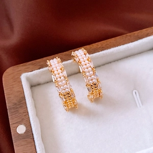 Detailed macro of 18K gold plated C-shaped earrings with pearls and zircon in a jewelry box