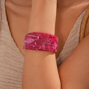 Detailed close-up of a wide fuchsia marble acrylic bangle on a model wrist