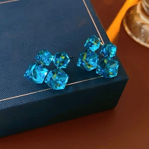 Macro shot of sea blue cube crystal earrings on a textured navy jewelry box display