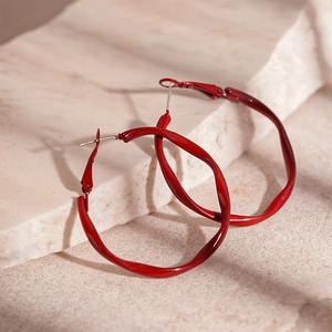 Detail view of twisted deep red lacquered hoop earrings on elegant white stone background