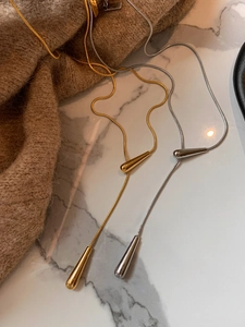 Artistic detail of gold and silver waterdrop pendant necklaces on marble and knitwear