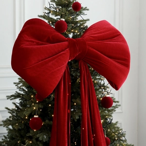 Giant burgundy velvet bow ornament on a Christmas tree with warm festive lights