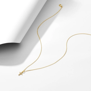 Macro detail of gold cross pendant with cubic zirconia on a minimalist cable chain