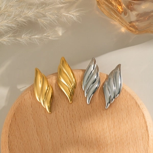 Textured leaf-shaped stainless steel earrings in gold and silver finish on a wooden tray