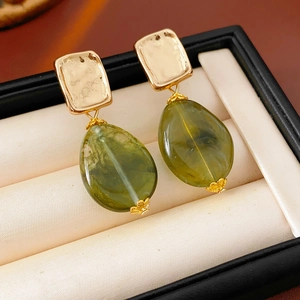 Close-up of vintage gold square stud earrings with green teardrop stone in a jewelry box