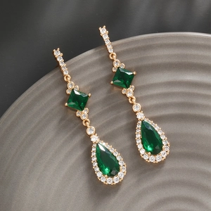 Macro detail of long drop earrings with emerald green gemstones and pave crystals