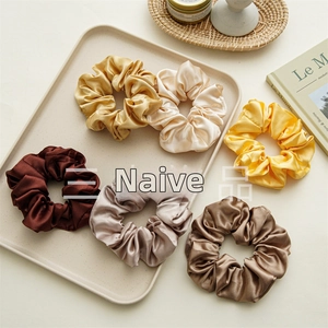Detailed close-up of six satin silk scrunchies in neutral earth tones with soft sheen