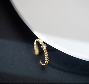 Detailed side view of a gold-plated twisted ring with a sparkling round zircon stone