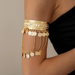 Detail of golden metal arm cuff featuring coin pendants and tassel chain fringes