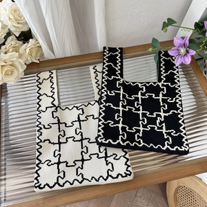 Close-up of knit tote bags with geometric puzzle patterns in black and cream white finish