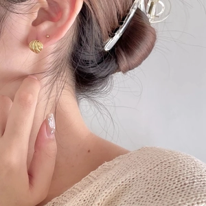 Close-up of golden geometric croissant stud earrings worn by a model in soft lighting