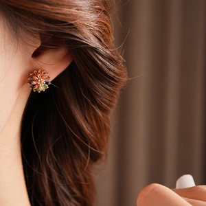 Close-up of a floral stud earring with colorful zircons on a golden base worn by a model