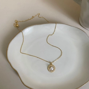 Elegant gold necklace with a white pearl and diamond-set round pendant on a ceramic tray