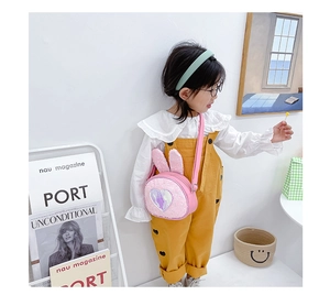 Pink plush bunny ear crossbody bag with sequins shown on child model in cozy indoor setting